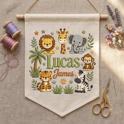 May include: A beige fabric wall hanging featuring a printed jungle theme with a lion, giraffe, elephant, monkey, tiger, and zebra. The text reads Lucas James in green and orange script. The banner is suspended from a wooden dowel with twine.