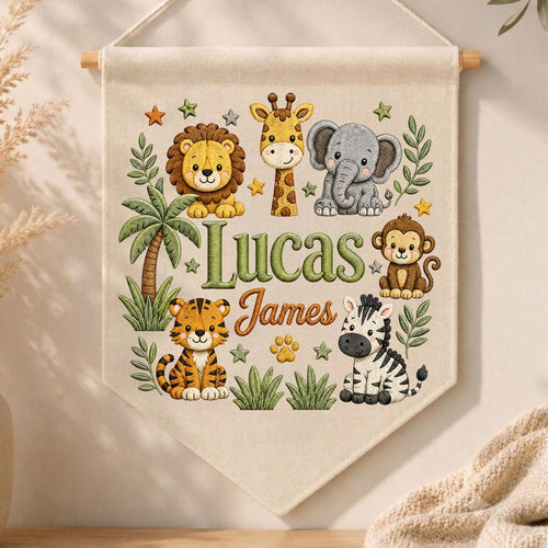 May include: A cream-colored fabric wall banner featuring embroidered illustrations of a lion, giraffe, elephant, monkey, tiger, and zebra. The text Lucas James is centered in green and orange script. The design includes palm trees and stars.