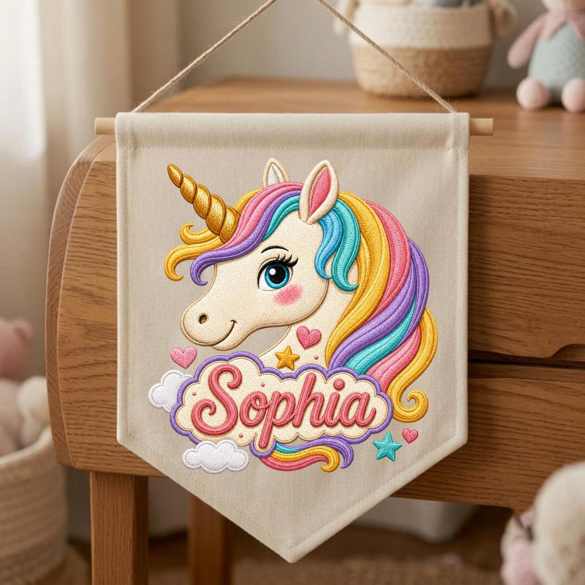 May include: A beige fabric wall banner featuring an embroidered unicorn head with a gold horn and a multi-colored mane in shades of pink, yellow, and blue. The name Sophia is embroidered in pink script below the unicorn, surrounded by small hearts, a star, and clouds.