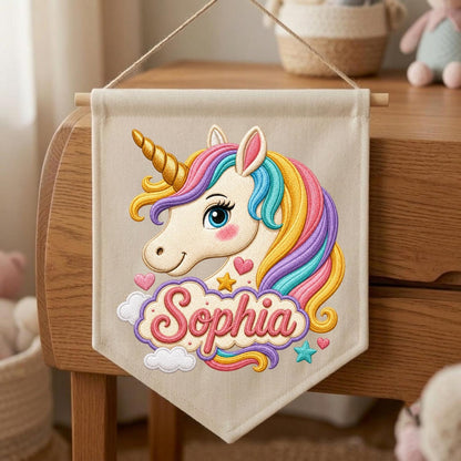 May include: A beige fabric wall banner featuring an embroidered unicorn head with a gold horn and a multi-colored mane in shades of pink, yellow, and blue. The name Sophia is embroidered in pink script below the unicorn, surrounded by small hearts, a star, and clouds.