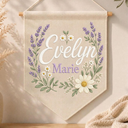 May include: A beige fabric wall banner featuring embroidered lavender sprigs and white daisies arranged in a wreath. The name Evelyn is stitched in large white script, with the name Marie embroidered below in smaller purple lettering.