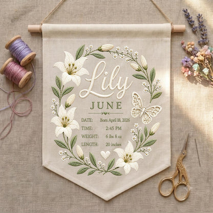 May include: A beige fabric wall hanging featuring embroidered white lily flowers, green leaves, and a butterfly. The text reads Lily, JUNE, DATE: April 18, 2026, TIME: 2:45 PM, WEIGHT: 6 lbs 8 oz, LENGTH: 20 inches. It hangs from a wooden rod with twine.
