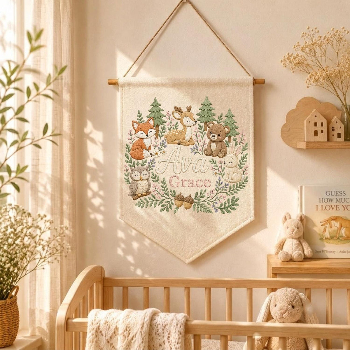 May include: A cream-colored fabric wall hanging banner featuring a printed illustration of a fox, deer, bear, owl, and rabbit surrounded by a green forest wreath. The name Ava Grace is printed in the center in a soft pink script font.