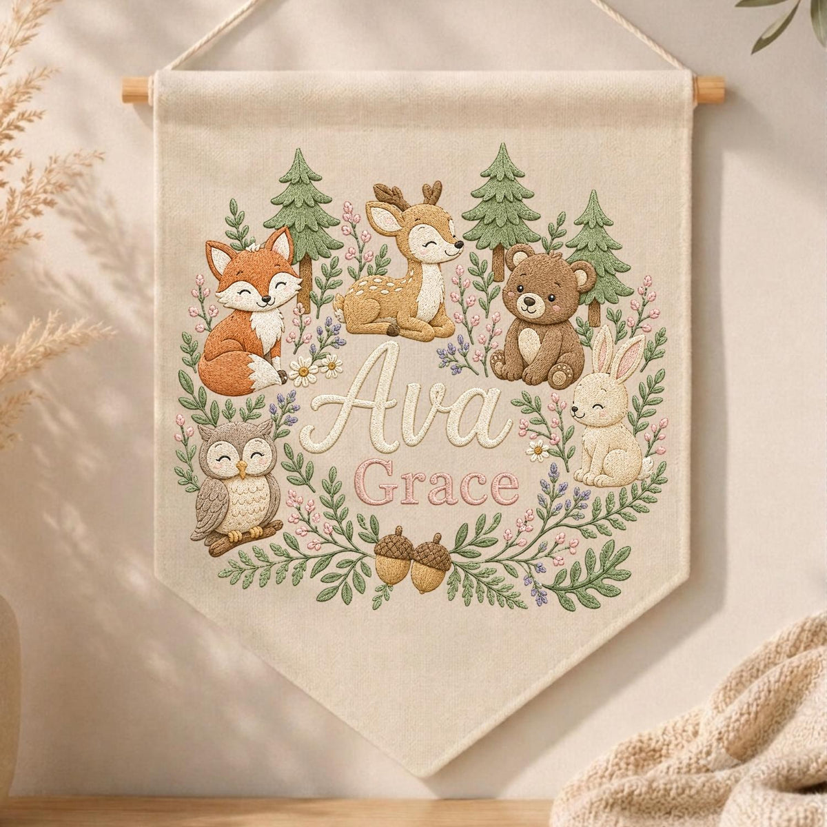 May include: A cream-colored fabric wall banner featuring an embroidered woodland scene with a fox, deer, bear, owl, and rabbit. The center displays the name Ava Grace in script and block lettering, surrounded by green pine trees and floral vines.