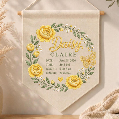 May include: A beige fabric wall hanging featuring a floral wreath of yellow peonies and green leaves. The text reads Daisy CLAIRE, DATE: April 18, 2026, TIME: 2:45 PM, WEIGHT: 6 lbs 8 oz, LENGTH: 20 inches, with a yellow butterfly and heart icon.