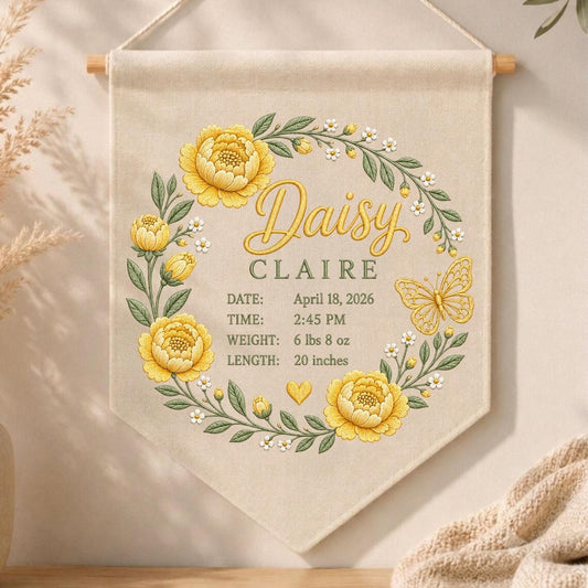 May include: A beige fabric wall hanging featuring a floral wreath of yellow peonies and green leaves. The text reads Daisy CLAIRE, DATE: April 18, 2026, TIME: 2:45 PM, WEIGHT: 6 lbs 8 oz, LENGTH: 20 inches, with a yellow butterfly and heart icon.