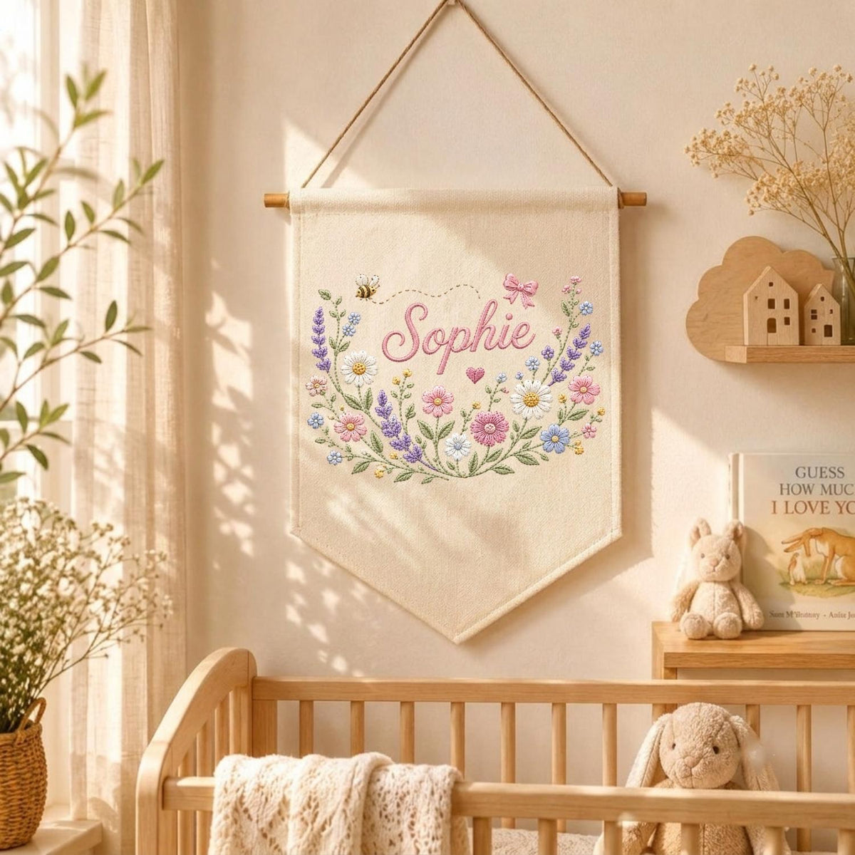 May include: A cream-colored fabric wall hanging banner featuring an embroidered floral wreath in shades of pink, purple, blue, and white. The name Sophie is stitched in pink cursive script in the center, accompanied by a small bee and a pink bow.