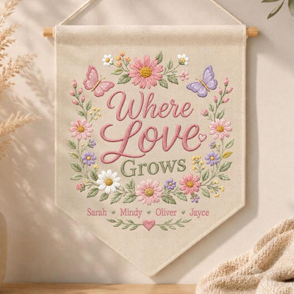 May include: A beige fabric wall banner featuring embroidered floral wreaths in pink, purple, and white with two butterflies. The text reads Where Love Grows, followed by the names Sarah, Mindy, Oliver, and Jayce, separated by small hearts.