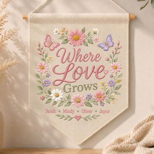 May include: A beige fabric wall banner featuring embroidered floral wreaths in pink, purple, and white with two butterflies. The text reads Where Love Grows, followed by the names Sarah, Mindy, Oliver, and Jayce, separated by small hearts.