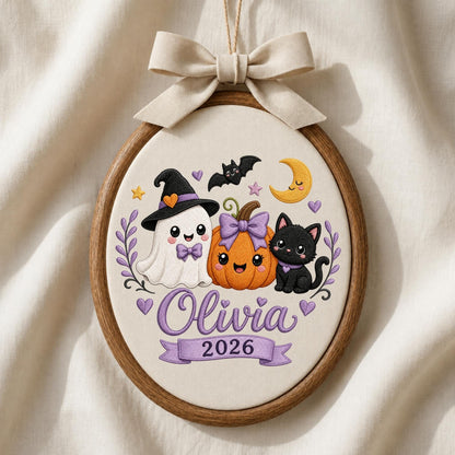 May include: An oval embroidery hoop featuring a white fabric background with a ghost wearing a witch hat, a pumpkin with a purple bow, and a black cat. The design includes a yellow crescent moon, stars, hearts, and the text Olivia 2026.