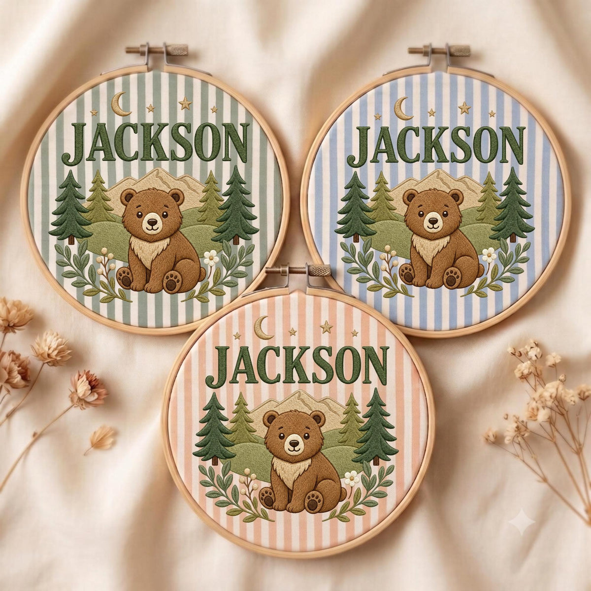 May include: Three circular embroidery hoops featuring a brown bear sitting in a forest with mountains, a crescent moon, and stars. Each hoop displays the name JACKSON in green text over a striped background in shades of green, blue, or peach.