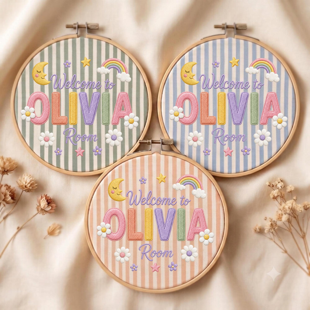 May include: Three circular wooden embroidery hoops featuring fabric with vertical stripes in sage green, light blue, and peach. Each hoop displays embroidered text reading Welcome to OLIVIA Room, accented with a crescent moon, rainbow, and flowers.