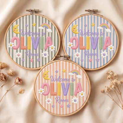 May include: Three circular wooden embroidery hoops featuring fabric with vertical stripes in sage green, light blue, and peach. Each hoop displays embroidered text reading Welcome to OLIVIA Room, accented with a crescent moon, rainbow, and flowers.