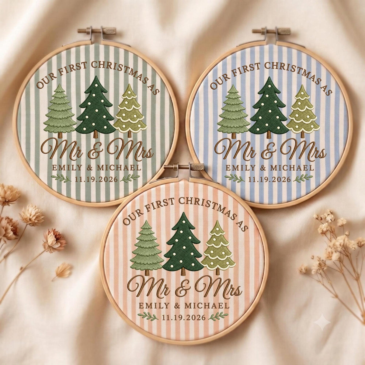 May include: Three circular wooden embroidery hoops featuring fabric with vertical stripes in sage green, light blue, and peach. Each displays embroidered Christmas trees, the text "OUR FIRST CHRISTMAS AS Mr &amp; Mrs EMILY &amp; MICHAEL 11.19.2026".