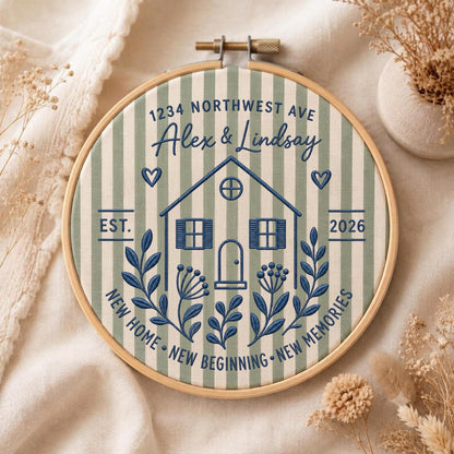 May include: A circular wooden embroidery hoop containing fabric with vertical sage green and white stripes. The fabric features dark blue embroidery of a house, floral sprigs, hearts, and the text 1234 NORTHWEST AVE, Alex &amp; Lindsay, EST. 2026, NEW HOME NEW BEGINNING NEW MEMORIES.