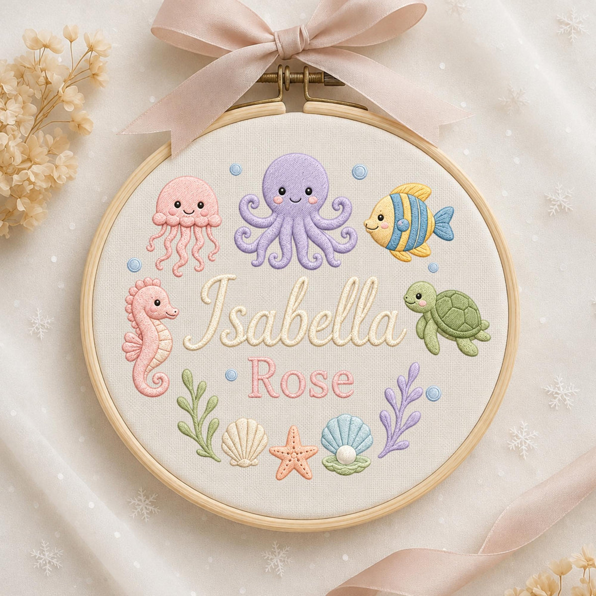 May include: A circular wooden embroidery hoop featuring a light-colored fabric background with embroidered sea creatures including a pink jellyfish, purple octopus, yellow fish, pink seahorse, and green turtle. The text Isabella Rose is centered.