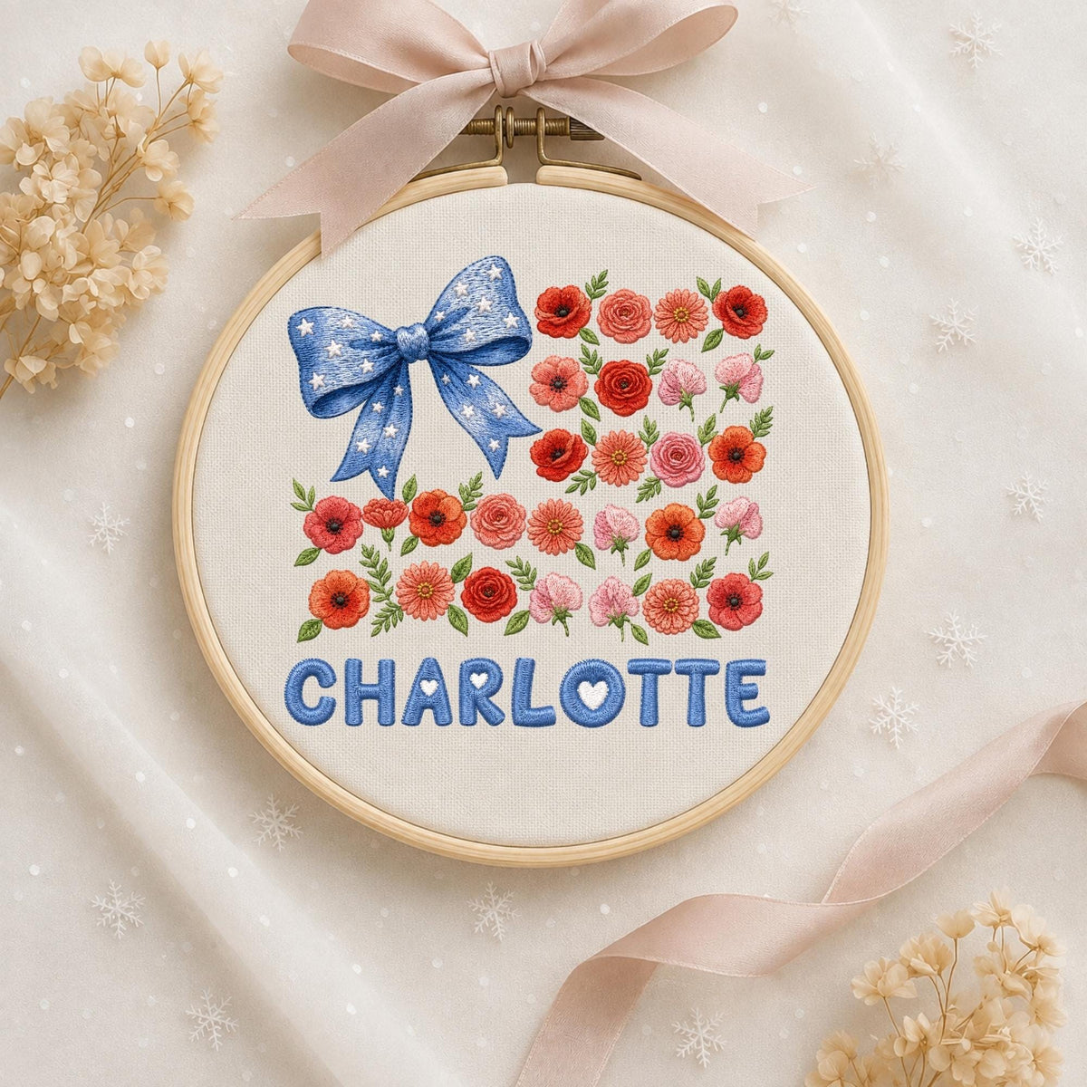May include: A circular wooden embroidery hoop containing white fabric with a hand-stitched design. The design features a blue bow with white stars, various red and pink flowers with green leaves, and the name CHARLOTTE in blue block letters.