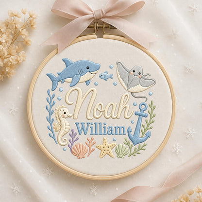 May include: A round wooden embroidery hoop containing fabric with a stitched ocean theme. The design features a blue shark, a stingray, a seahorse, a starfish, seashells, and an anchor. The names Noah and William are embroidered in the center.