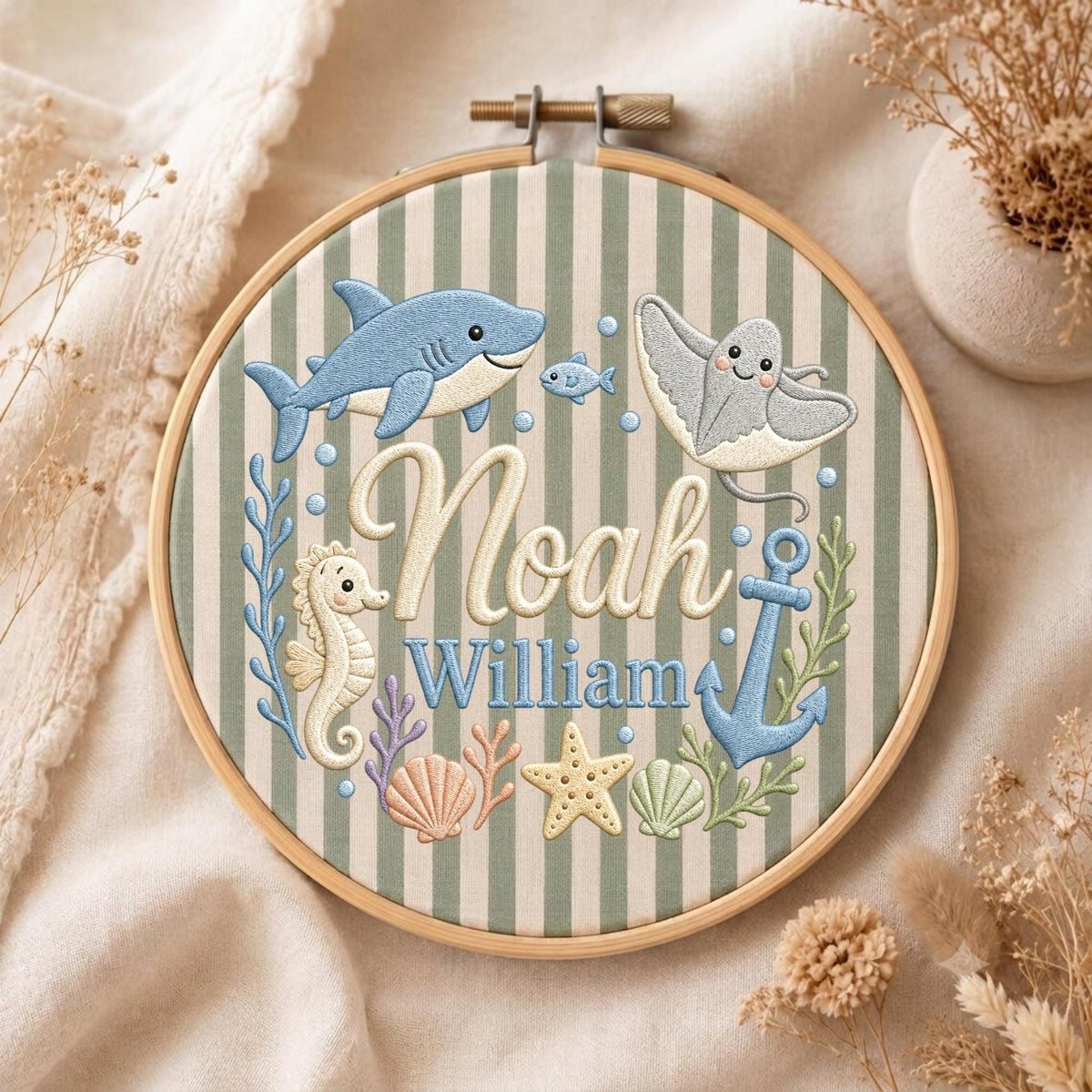 May include: A circular wooden embroidery hoop containing fabric with vertical sage green and white stripes. The embroidery features a blue shark, a stingray, a seahorse, an anchor, seashells, and a starfish, with the names Noah and William.