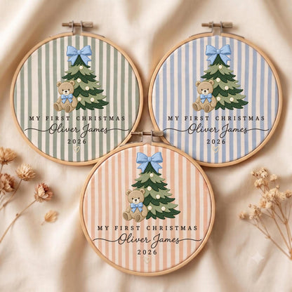 May include: Three circular wooden embroidery hoops featuring striped fabric in sage green, light blue, and peach. Each displays an embroidered Christmas tree with a light blue bow, a teddy bear, and the text MY FIRST CHRISTMAS Oliver James 2026.