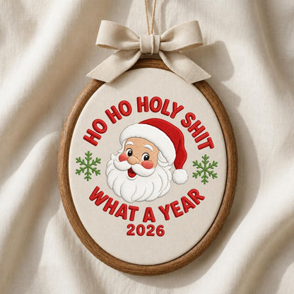 May include: An oval wooden embroidery hoop containing off-white fabric with an embroidered Santa Claus face, green snowflakes, and the red text HO HO HOLY SHIT WHAT A YEAR 2026. A beige fabric bow is attached to the top of the wooden frame.