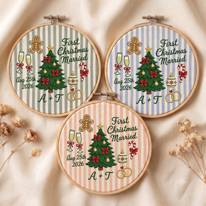 May include: Three circular wooden embroidery hoops featuring striped fabric backgrounds in sage green, light blue, and peach. Each displays a Christmas tree, gingerbread man, champagne flutes, candy cane, ornament, and rings with the text First Christmas Married Aug 25th 2026 A + T.