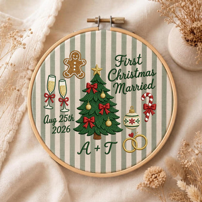 May include: A round wooden embroidery hoop containing fabric with green and white vertical stripes. The embroidery features a Christmas tree, a gingerbread man, two champagne flutes, a candy cane, and two gold rings. Text reads: First Christmas Married, Aug 25th 2026, and A + T.