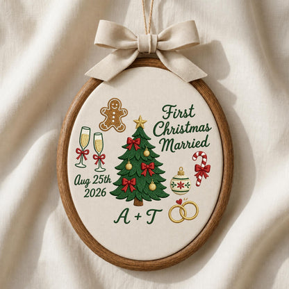 May include: An oval embroidery hoop ornament featuring a beige fabric background with a cream-colored ribbon bow at the top. The design includes a green Christmas tree, a gingerbread man, champagne flutes, a candy cane, and two gold rings. Text reads First Christmas Married, Aug 25th 2026, and A + T.