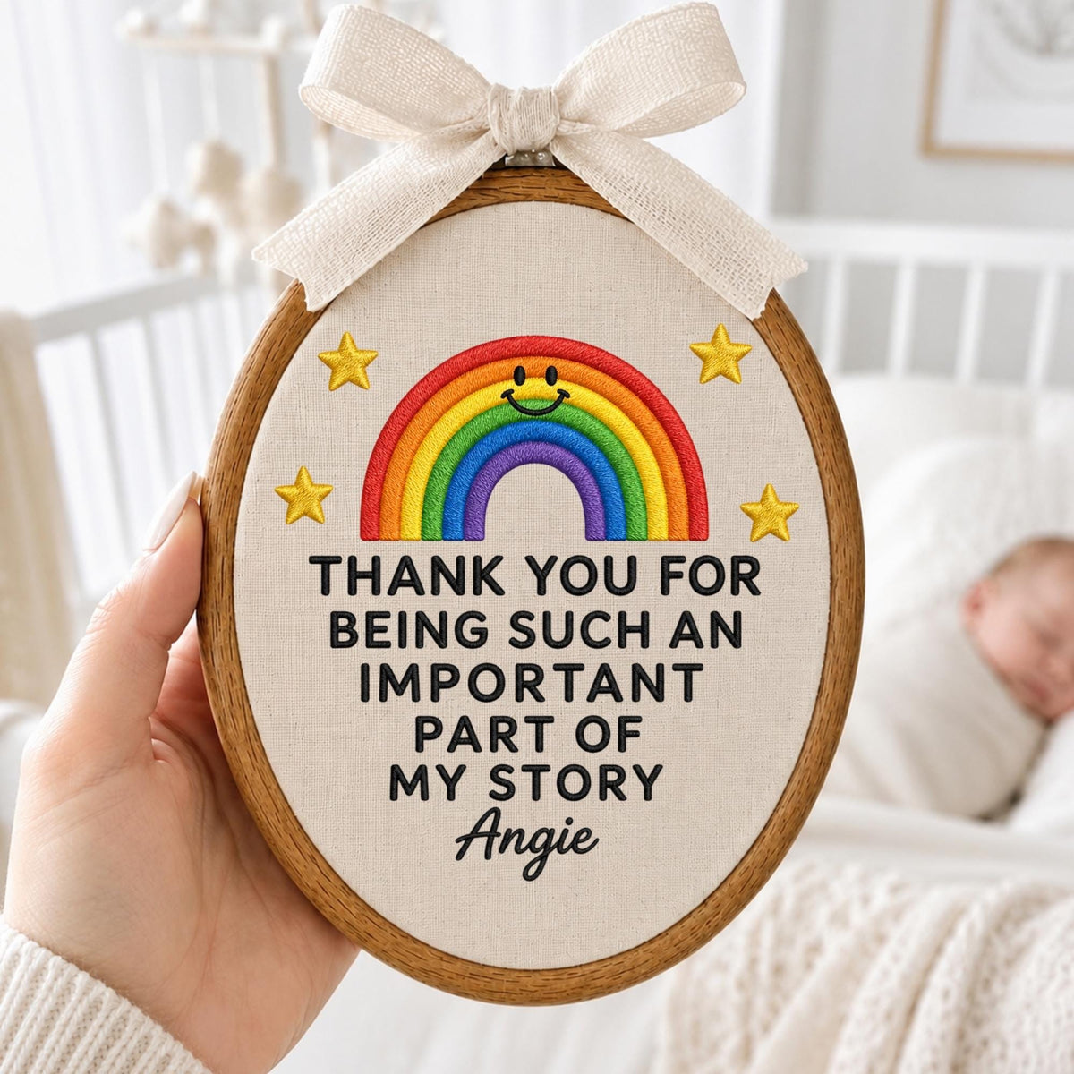 May include: An oval embroidery hoop featuring a cream fabric background with a stitched rainbow, four yellow stars, and the black text: THANK YOU FOR BEING SUCH AN IMPORTANT PART OF MY STORY Angie. A beige ribbon bow is tied at the top of the hoop.