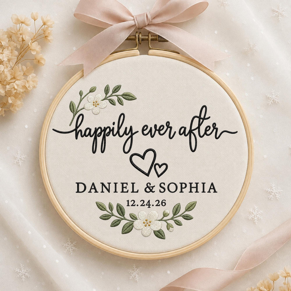 May include: A round wooden embroidery hoop containing white fabric with black embroidered text that reads "happily ever after", "DANIEL &amp; SOPHIA", and "12.24.26". The design includes two small hearts and floral sprigs with white flowers.