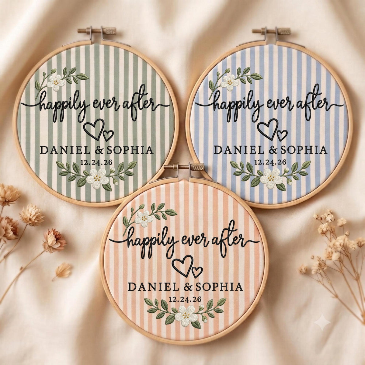 May include: Three circular wooden embroidery hoops featuring fabric with vertical stripes in sage green, light blue, and peach. Each hoop displays the text "happily ever after", "DANIEL &amp; SOPHIA", and "12.24.26" with floral accents and two hearts.