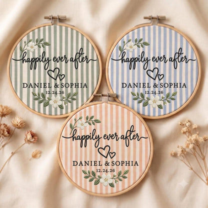 May include: Three circular wooden embroidery hoops featuring fabric with vertical stripes in sage green, light blue, and peach. Each hoop displays the text "happily ever after", "DANIEL &amp; SOPHIA", and "12.24.26" with floral accents and two hearts.