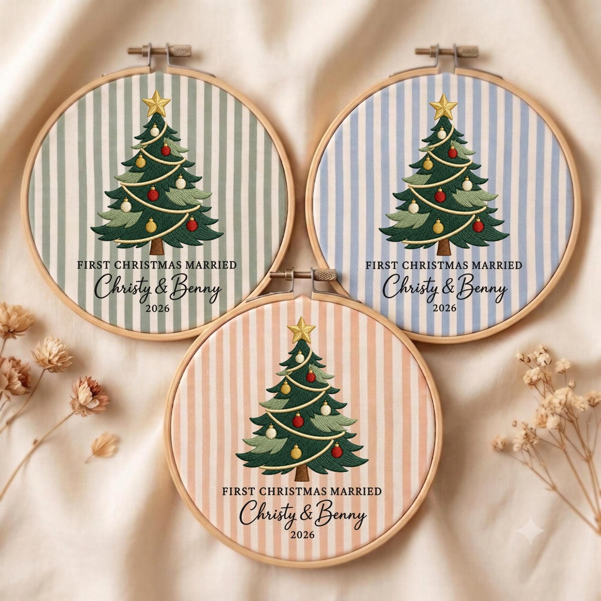 May include: Three circular embroidery hoops featuring striped fabric in sage green, light blue, and peach. Each hoop displays a central embroidered Christmas tree with a gold star, red and yellow ornaments, and the text FIRST CHRISTMAS MARRIED Christy &amp; Benny 2026.