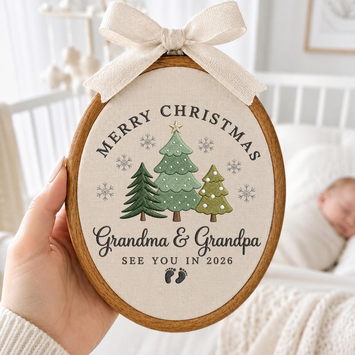 May include: An oval embroidery hoop featuring a beige fabric background with a cream-colored ribbon bow at the top. The design includes three embroidered green Christmas trees, grey snowflakes, and the text Merry Christmas, Grandma &amp; Grandpa, SEE YOU IN 2026, and two small baby footprints.