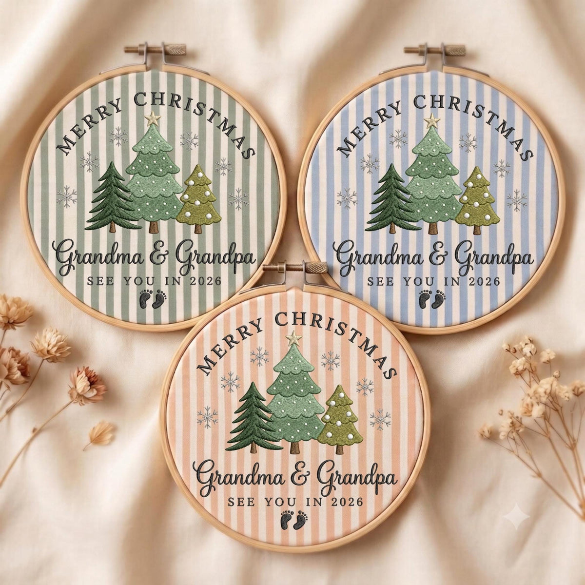 May include: Three circular embroidery hoops featuring striped fabric in sage green, light blue, and peach. Each hoop displays embroidered Christmas trees, snowflakes, and the text Merry Christmas Grandma &amp; Grandpa SEE YOU IN 2026 with baby footprints.