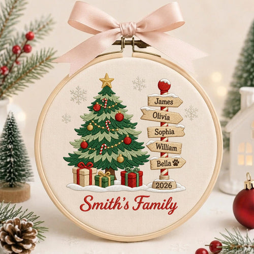 May include: A circular embroidery hoop featuring a stitched Christmas tree, wrapped gifts, and a signpost with the names James, Olivia, Sophia, William, and Bella, plus the year 2026. The text Smith's Family is embroidered below, topped with a pink bow.