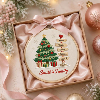 May include: A round embroidery hoop featuring a Christmas tree, wrapped gifts, and a signpost with the names James, Olivia, Sophia, William, and Bella, plus the year 2026 and the text Smith's Family, topped with a light pink satin ribbon bow.