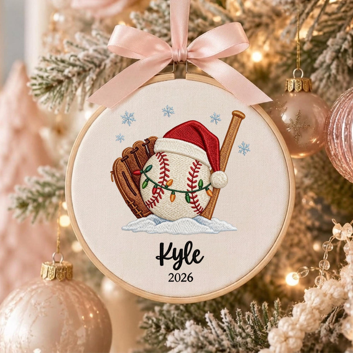 May include: A round embroidery hoop ornament featuring a baseball with a red Santa hat and string lights, a brown baseball glove, and a wooden bat. The design includes blue snowflakes, the name Kyle, and the year 2026, topped with a light pink ribbon.