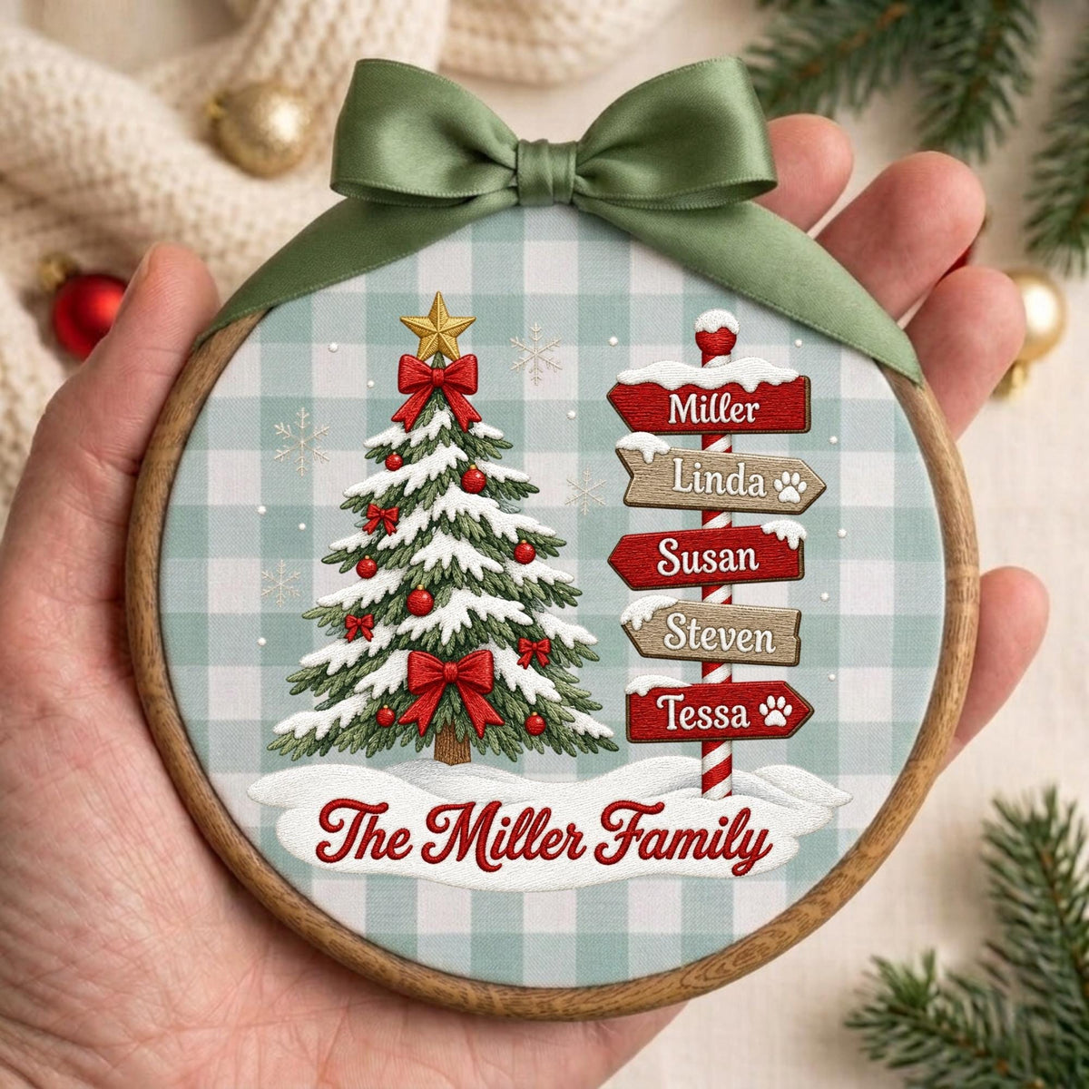 May include: A round wooden Christmas ornament featuring a light blue and white buffalo check background. It displays a decorated pine tree with red bows and a signpost with the names Miller, Linda, Susan, Steven, and Tessa. The text The Miller Family is printed at the bottom, topped with a green satin ribbon.
