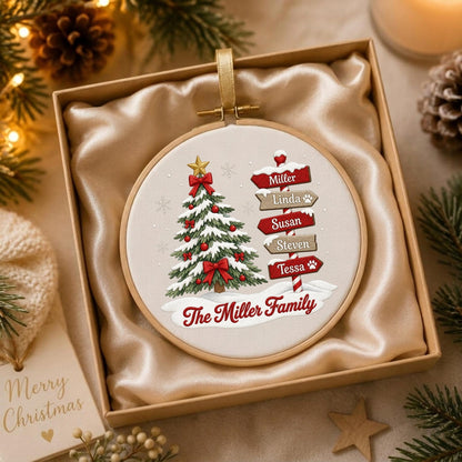 May include: A round embroidery hoop ornament featuring a printed Christmas tree with red bows and a signpost with the names Miller, Linda, Susan, Steven, and Tessa, plus the text The Miller Family, all set against a light fabric background.