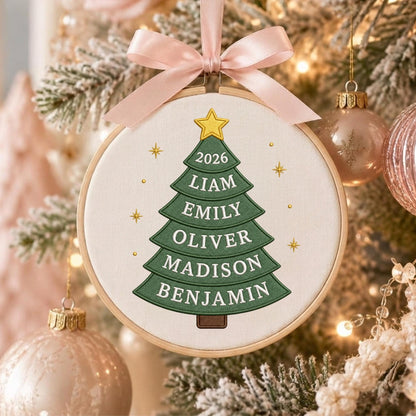 May include: A round wooden embroidery hoop ornament featuring a green fabric Christmas tree with a yellow star on top. The tree displays the year 2026 and the names Liam, Emily, Oliver, Madison, and Benjamin in white text. A light pink ribbon bow is attached.