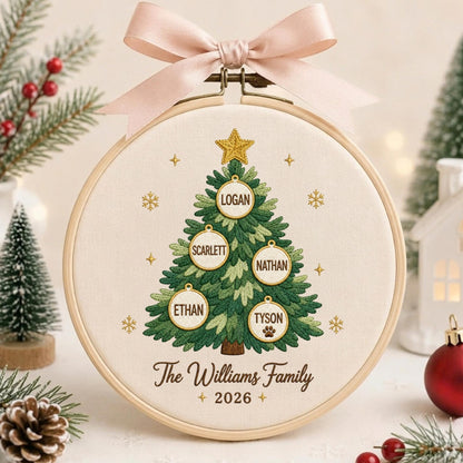 May include: A circular wooden embroidery hoop containing a cream-colored fabric with a stitched green Christmas tree. The tree features five white circular ornaments with the names Logan, Scarlett, Nathan, Ethan, and Tyson, topped with a gold star.