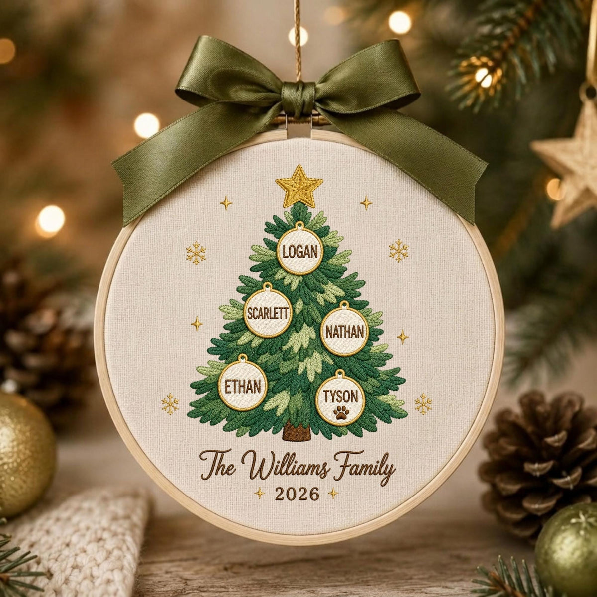 May include: A round embroidery hoop ornament featuring a stitched green Christmas tree with five circular ornaments labeled Logan, Scarlett, Nathan, Ethan, and Tyson. The text The Williams Family 2026 is embroidered below, topped with a dark green satin bow.