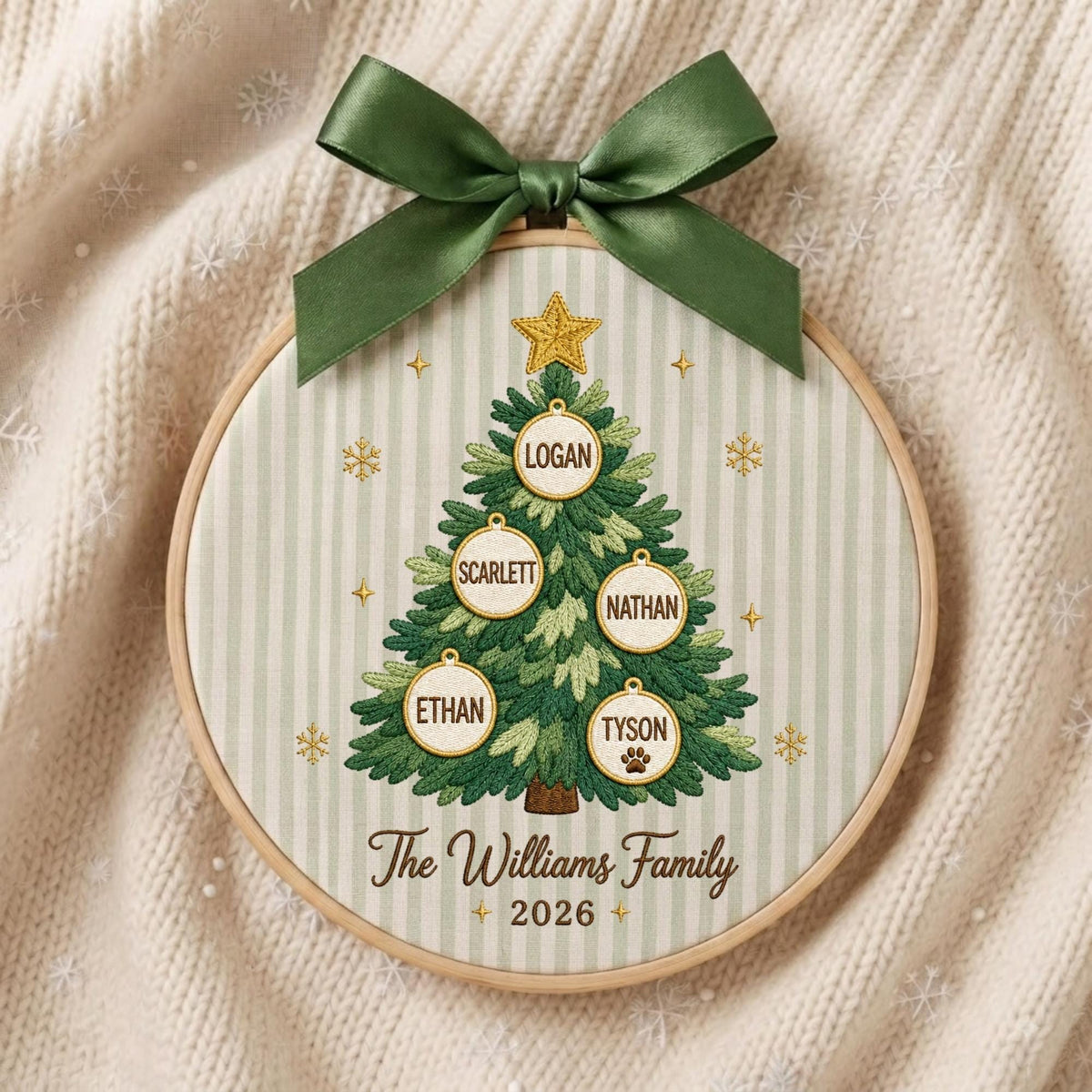 May include: A circular embroidery hoop featuring a green Christmas tree design on a light green striped fabric. The tree is decorated with a gold star and five white ornaments labeled Logan, Scarlett, Nathan, Ethan, and Tyson. Text reads The Williams Family 2026.