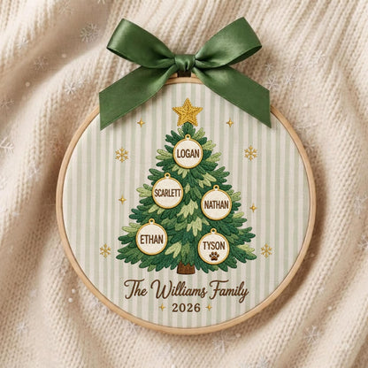 May include: A circular embroidery hoop featuring a green Christmas tree design on a light green striped fabric. The tree is decorated with a gold star and five white ornaments labeled Logan, Scarlett, Nathan, Ethan, and Tyson. Text reads The Williams Family 2026.