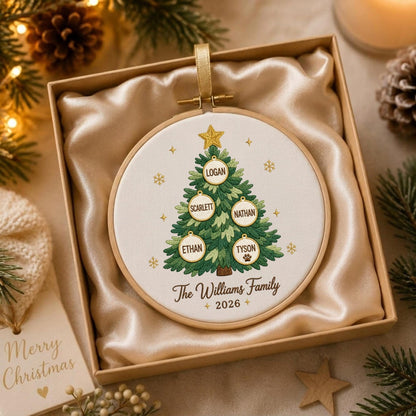 May include: A round wooden embroidery hoop containing a white fabric panel with an embroidered green Christmas tree. The tree features five circular ornaments with the names Logan, Scarlett, Nathan, Ethan, and Tyson, plus the text The Williams Family 2026.