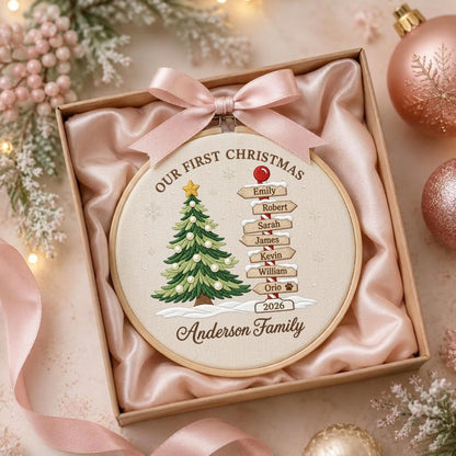 May include: A round wooden embroidery hoop containing fabric with a Christmas tree and a signpost featuring the names Emily, Robert, Sarah, James, Kevin, William, Orio, and the text Our First Christmas 2026 Anderson Family, topped with a pink ribbon.