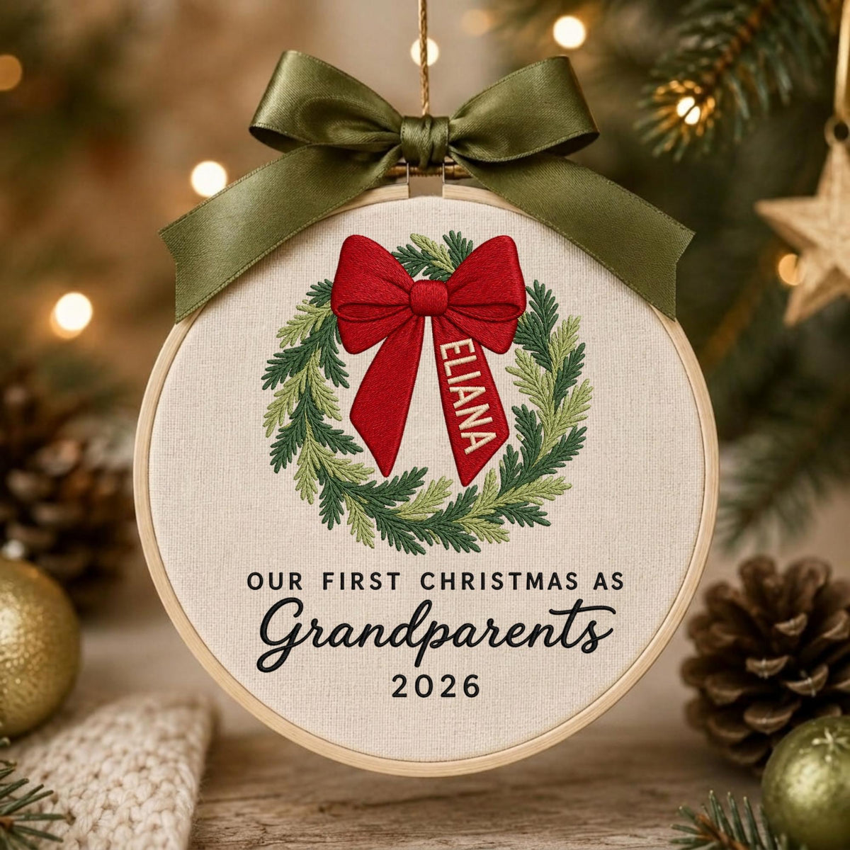 May include: A round wooden embroidery hoop ornament featuring a cream fabric background. It displays an embroidered green wreath with a large red bow, which includes the name ELIANA. Text reads OUR FIRST CHRISTMAS AS Grandparents 2026.