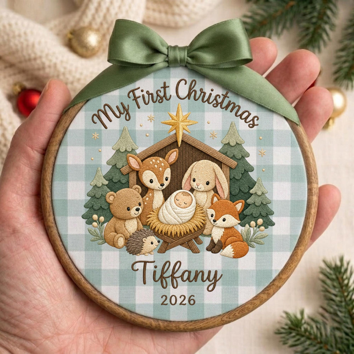 May include: A round wooden embroidery hoop ornament featuring a light blue and white buffalo check fabric background. The design shows a baby in a manger surrounded by a deer, bear, rabbit, fox, and hedgehog, with the text My First Christmas Tiffany 2026.