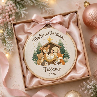 May include: A round embroidery hoop ornament featuring a beige fabric center with a printed illustration of a baby in a manger surrounded by a bear, deer, hedgehog, rabbit, and fox. Text reads My First Christmas, Tiffany, and 2026.